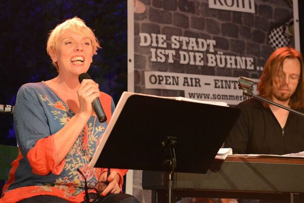 Anne Rixmann sitzt auf der Bühne und singt ins Mikro. Friso Lücht spielt rechts neben ihr am E-Piano