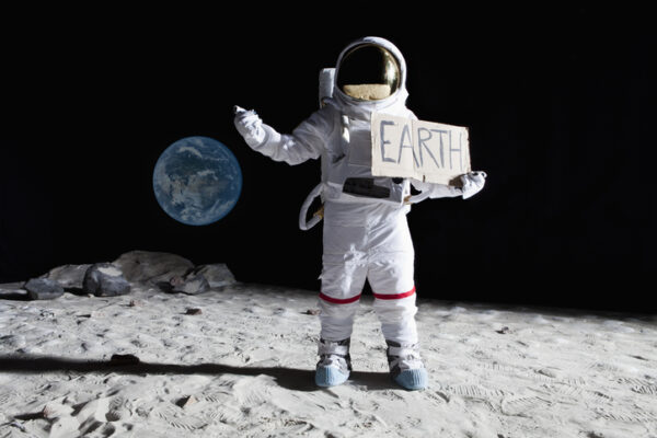 Ein Astronaut steht auf dem Mond, im Hintergrund die Erde. Er hält ein Schild "Earth"